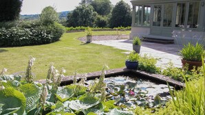 A garden with a pond, potted plants, and a conservatory. - Foxholes Barn (Kidderminster)