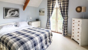 Ein Schlafzimmer mit Bett, Nachttisch, Kommode, einem Fenster mit Vorhängen und einem Wandbild.