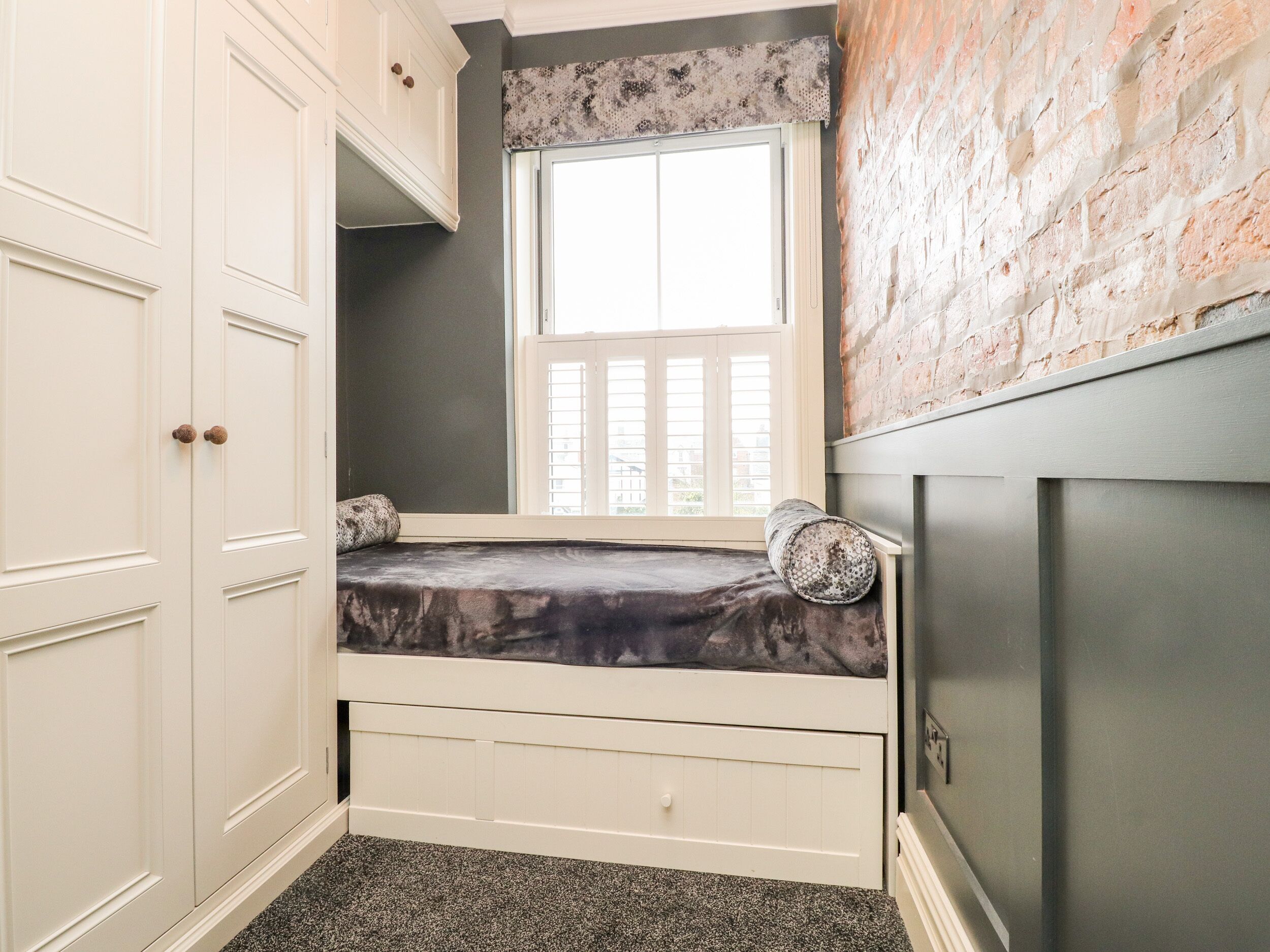 Un dormitorio pequeño con ventana, cama, armario y pared de ladrillo.