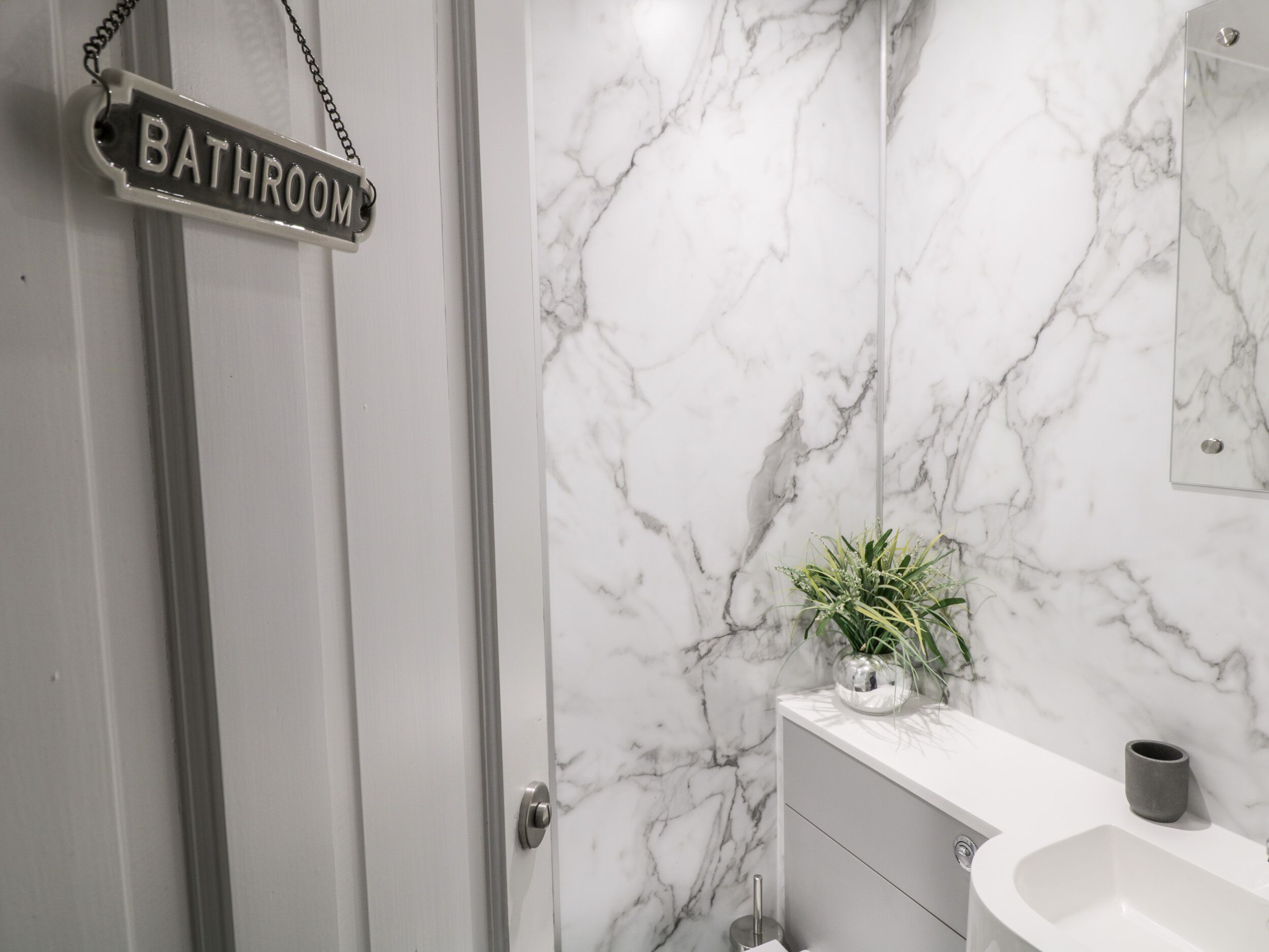 A bathroom with a marble wall, a sink, a mirror, and a potted plant.