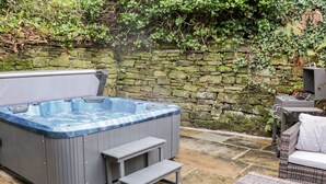 Un bain à remous avec des marches, des meubles en osier et un mur en pierre.