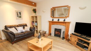Una sala de estar con un sofá de cuero, una mesa de centro de madera, una chimenea, un televisor y una estantería.