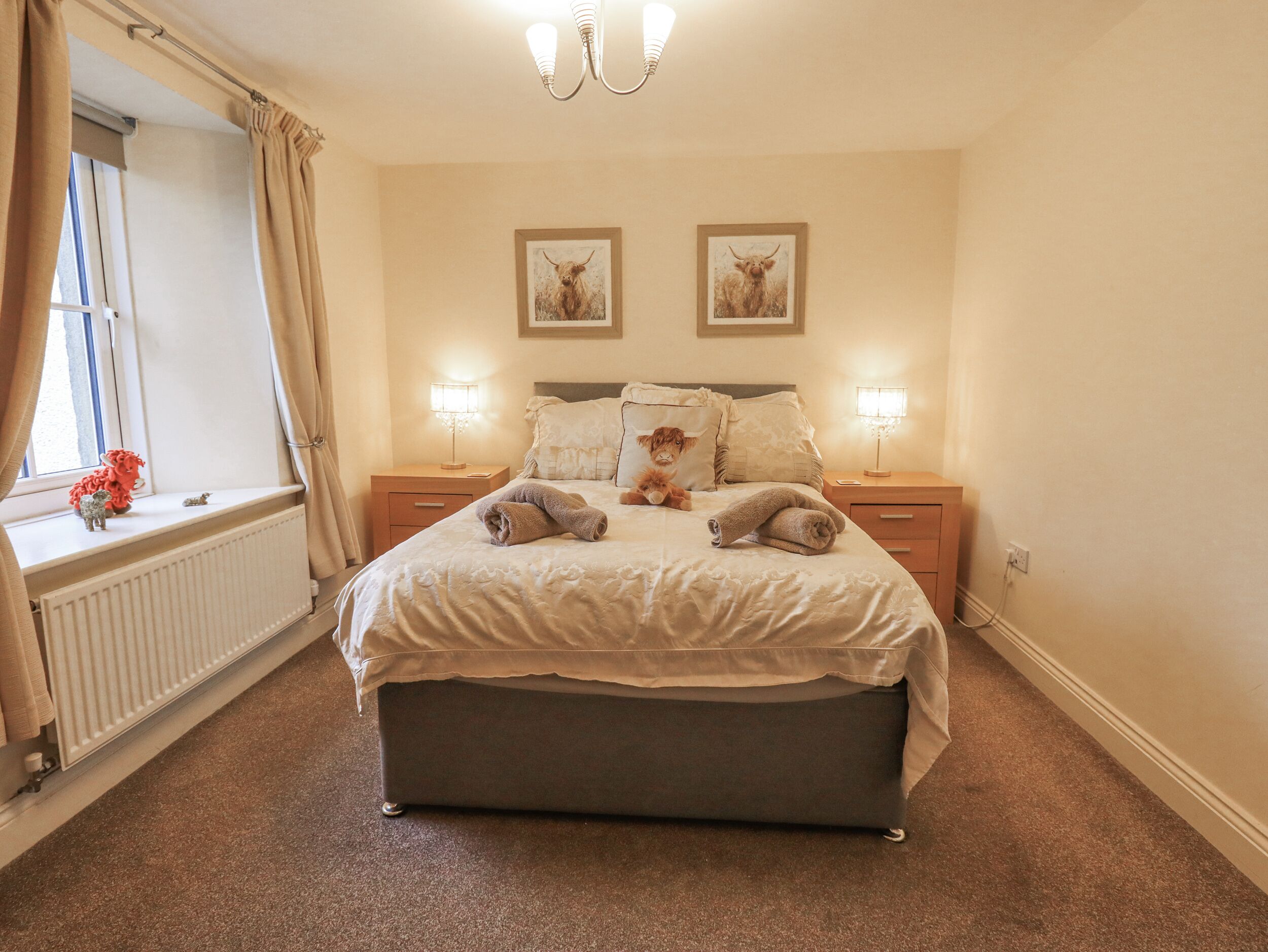A neatly arranged bedroom with a large bed, two bedside tables, a window with curtains, and two framed pictures on the wall.