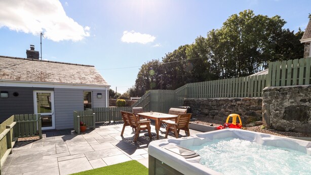 Un jardin avec un jacuzzi, une table de patio entourée de chaises, un petit potager et un mur en pierre.