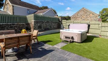A backyard with a hot tub, a wooden table with chairs, and a stone wall.