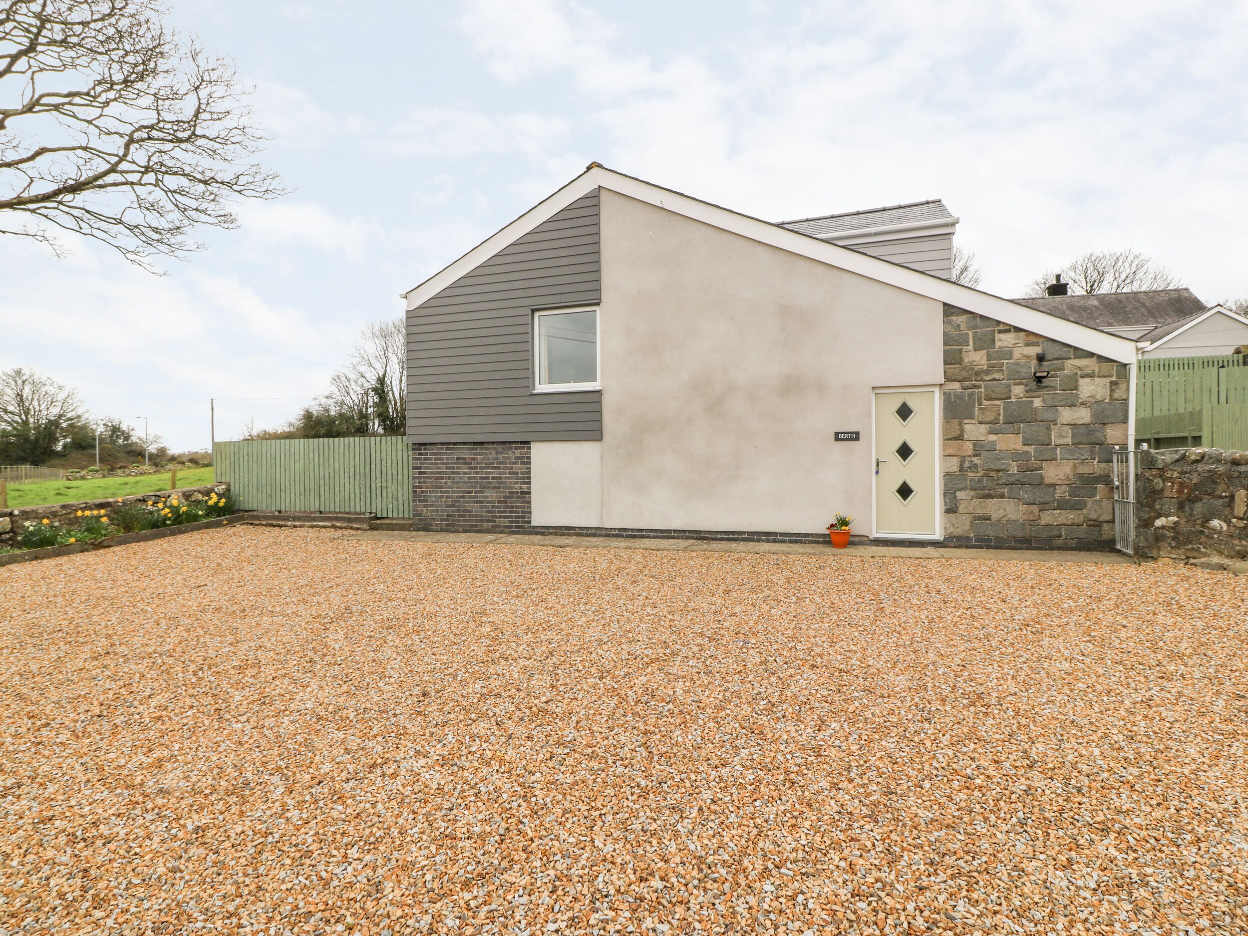 A modern two-story house with a gravel driveway, a stone wall, and a green fence.