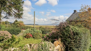A rural landscape with a house, lush garden, and a clear sky. - Westmorland Cottage (Grange-over-Sands)
