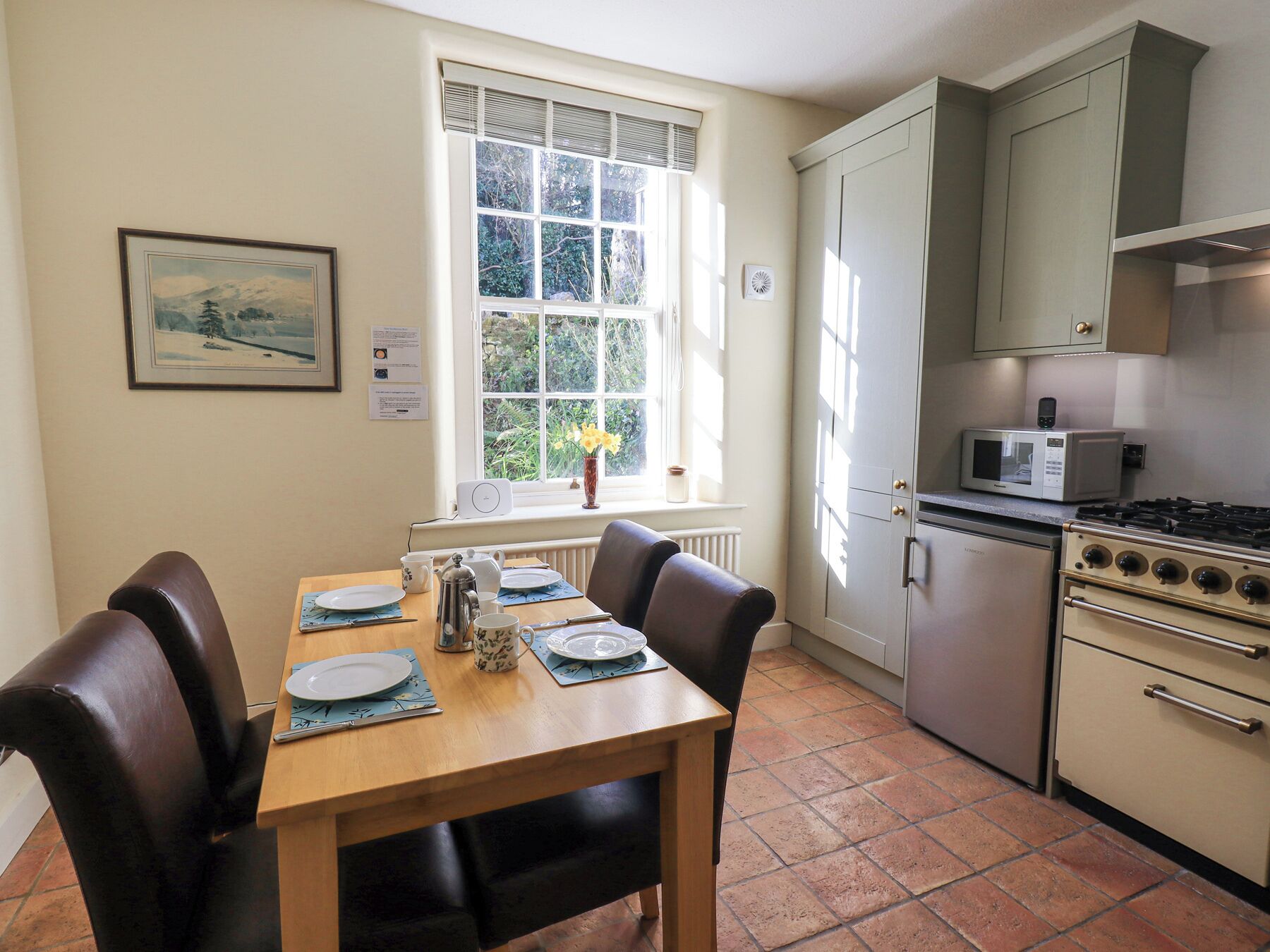A compact kitchen with a dining table, chairs, a stove, a microwave, and a window with a view of greenery.