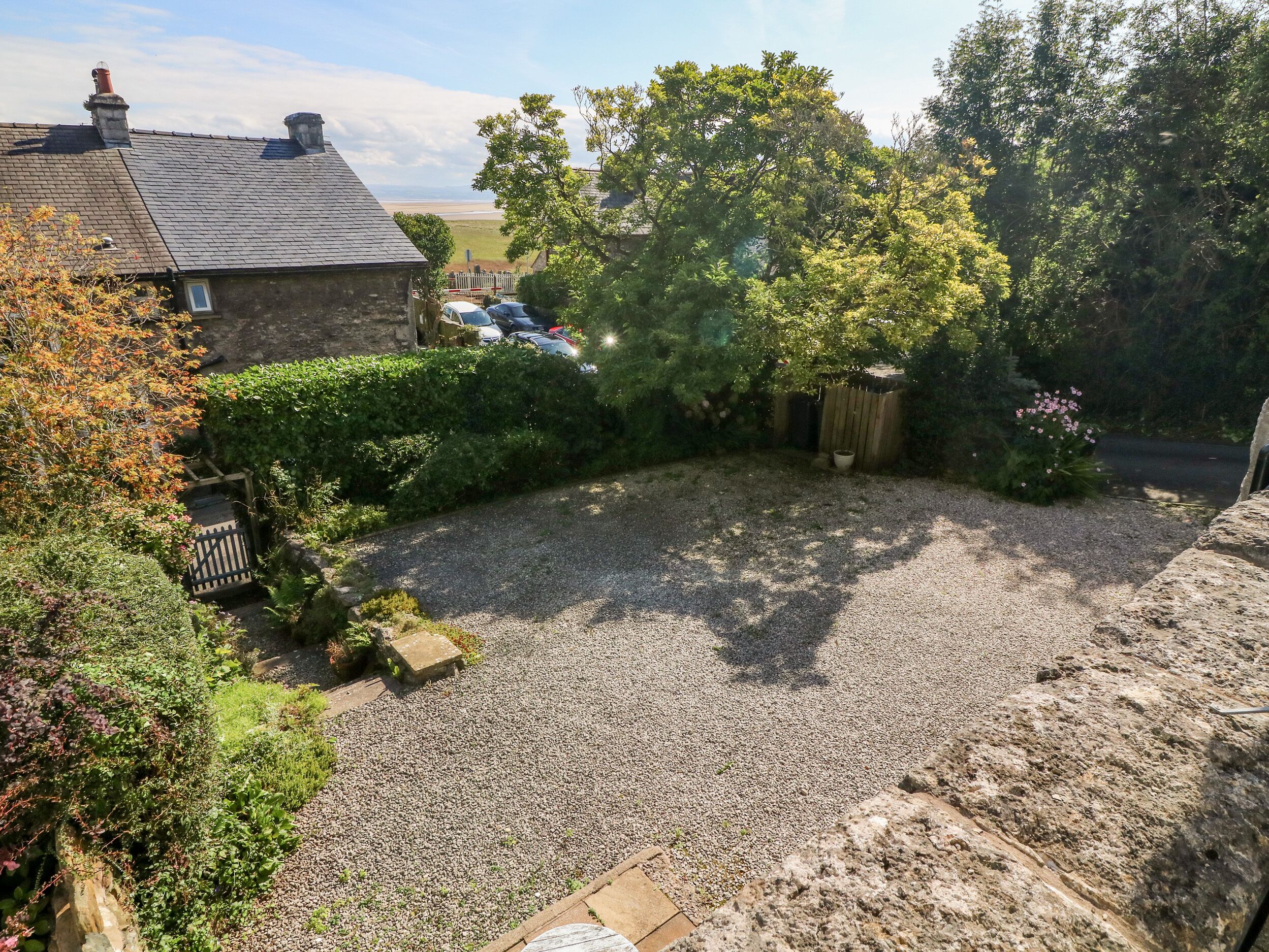 A gravel backyard with a stone wall, a wooden fence, and a large tree providing shade.