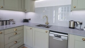 A kitchen with light green cabinets, a stainless steel sink, a black toaster, and a dishwasher. - Westmorland Cottage (Grange-over-Sands)