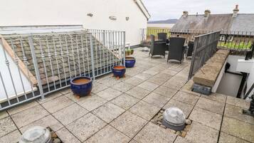 Um terraço no telhado com azulejos de pedra, dois vasos azuis, um lareira com cobertura de vidro e uma cerca de metal.
