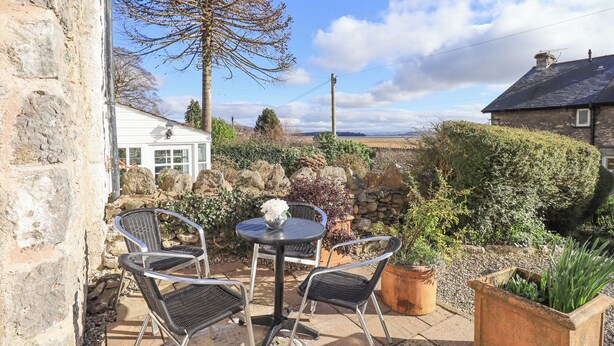 A patio with two metal chairs and a table, surrounded by stone walls and potted plants. - Westmorland Cottage (Grange-over-Sands)