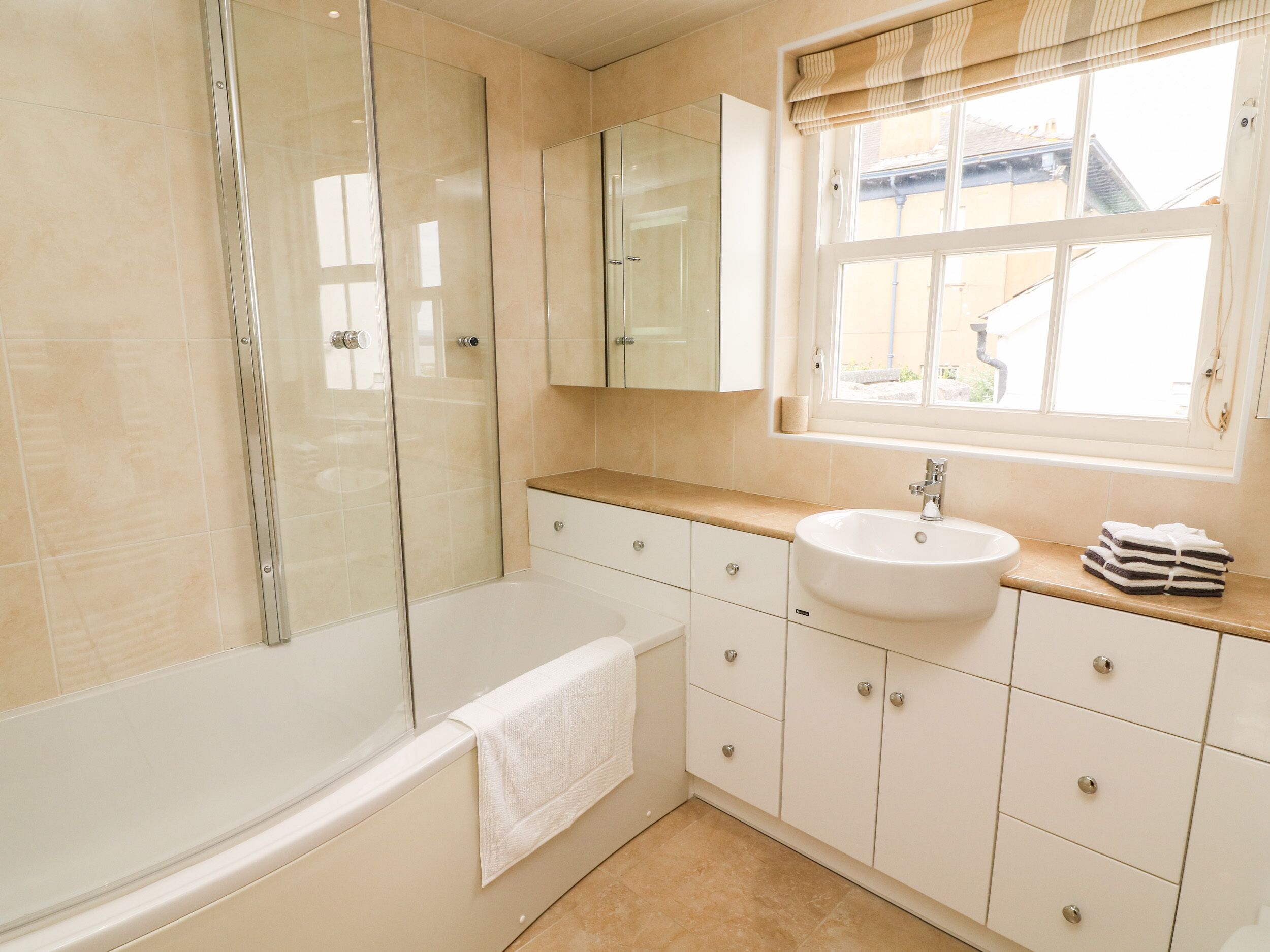 Un baño moderno con ducha acristalada, lavamanos blanco y tocador con cajones.