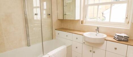 Un baño moderno con ducha acristalada, lavamanos blanco y tocador con cajones.