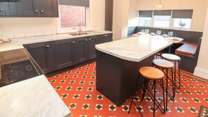 A modern kitchen with dark cabinets, a marble countertop, and a red and black patterned floor. - Livingstone House (Llandudno)