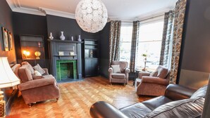 A living room with a fireplace, leather sofas, a chandelier, and a view of the outdoors. - Livingstone House (Llandudno)