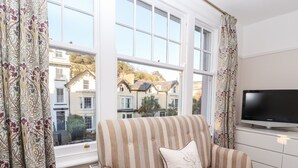 A striped sofa with a cushion, a flat-screen TV, and a window with curtains. - Livingstone House (Llandudno)