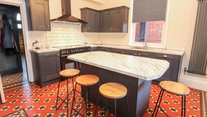 A modern kitchen with dark cabinets, a large island with stools, a gas stove, and a patterned floor. - Livingstone House (Llandudno)