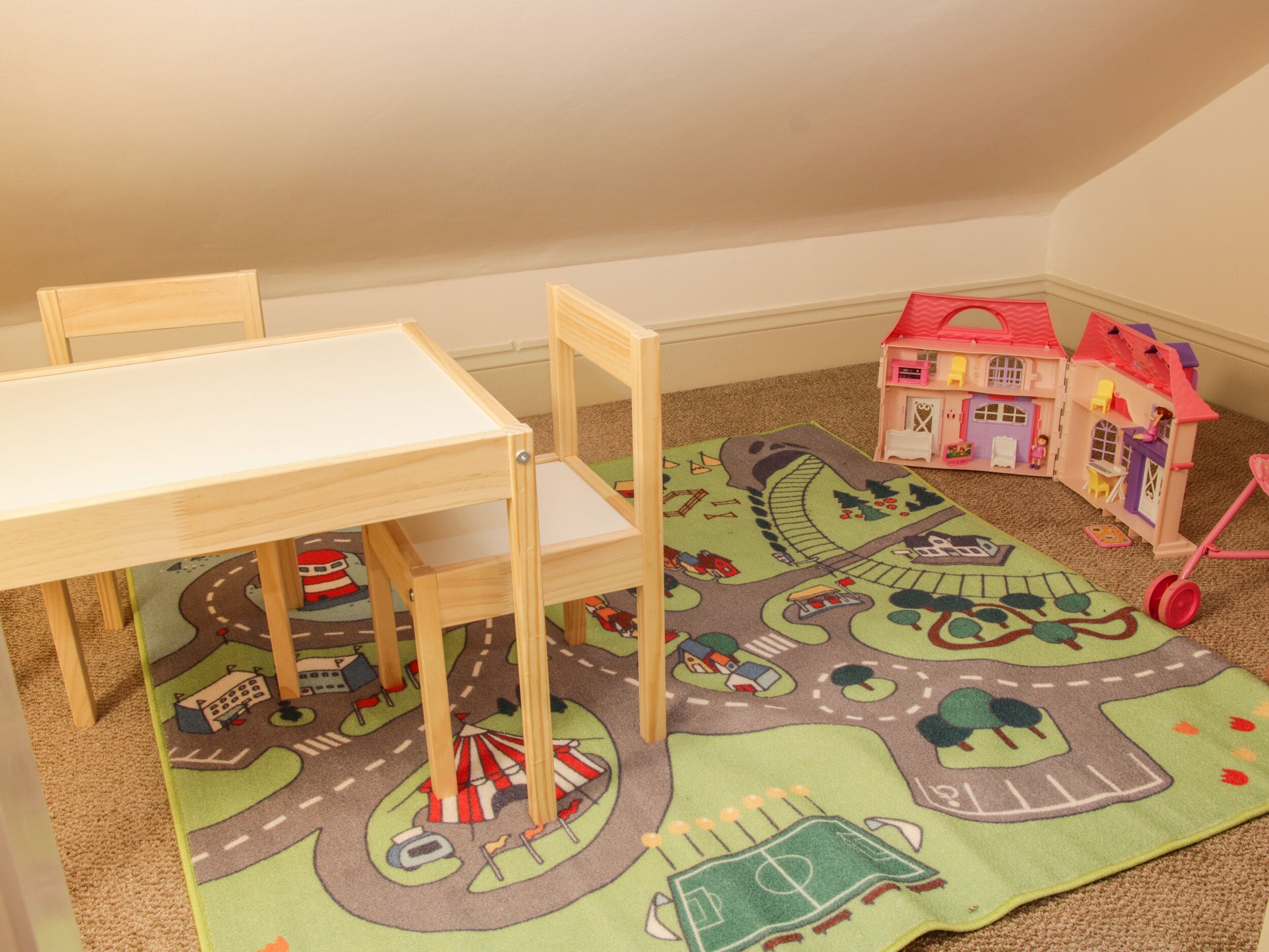 A child's play area with a small table, chairs, a colorful play mat, and a dollhouse.