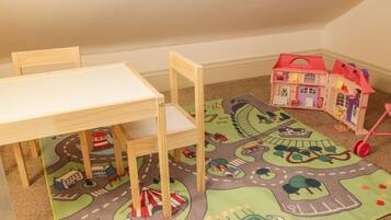 A child's play area with a small table, chairs, a colorful play mat, and a dollhouse.
