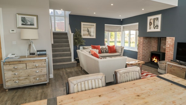 A modern living room with a fireplace, a sofa, a dining table, and a staircase leading to another level. - The Deck House (Chathill)