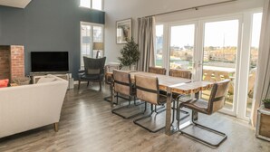 A spacious living room with a dining area, large windows, and a view of the outdoors. - The Deck House (Chathill)
