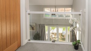 A room with a wooden door, a white ceiling, a hanging light fixture, a window with curtains, and a potted plant. - The Deck House (Chathill)