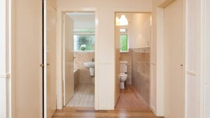 Un pasillo que conduce a un baño con inodoro, lavamanos y zona de ducha.