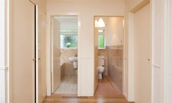 Un pasillo que conduce a un baño con inodoro, lavamanos y zona de ducha.