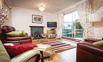 Un salón acogedor con chimenea, sofás de cuero, televisor y un amplio ventanal con cortinas.
