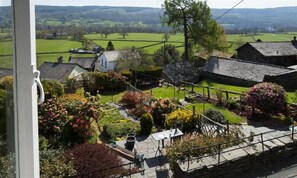 A rural village with stone houses, a garden with various plants, and a view of the surrounding countryside.