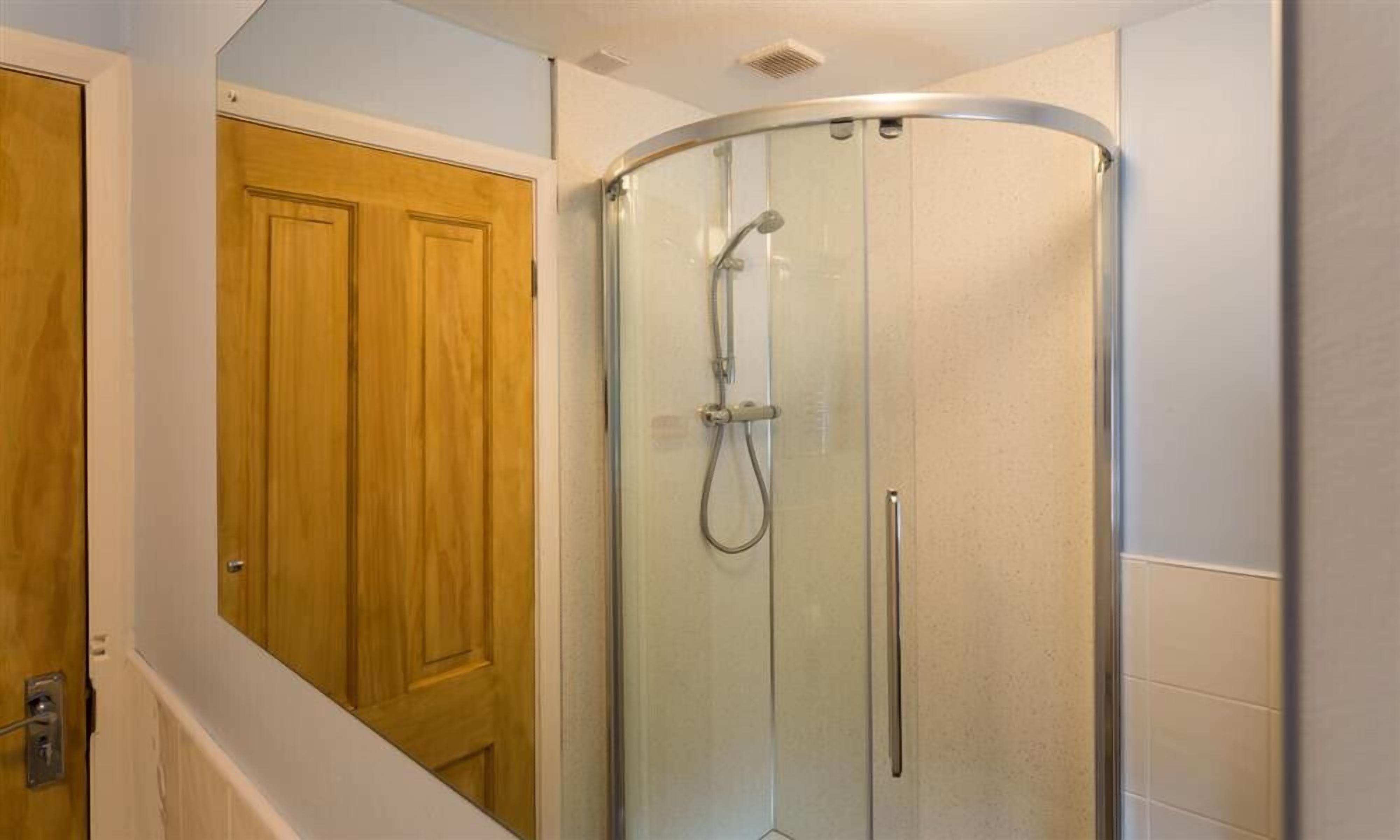 Un baño con ducha envuelta en cristal, puerta de madera y paredes de azulejos blancos.