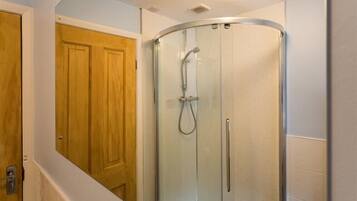 Un baño con ducha envuelta en cristal, puerta de madera y paredes de azulejos blancos.