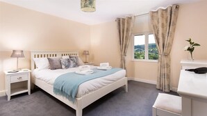 A bedroom with a bed, bedside tables, a desk, and a window with curtains. - Dormouse Cottage (Coniston)