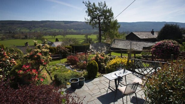 A patio with a table and chairs, surrounded by a garden with various plants and flowers. - Dormouse Cottage (Coniston)