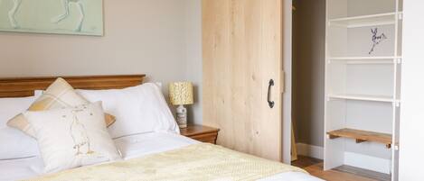 Un dormitorio con cama de madera, ropa de cama blanca, una mesita de noche con lámpara, un armario con puerta corredera y un cuadro en la pared con canguros.