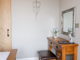 Quarto com cama de madeira, cômoda de madeira com espelho, um banquinho pequeno e um enfeite na parede.