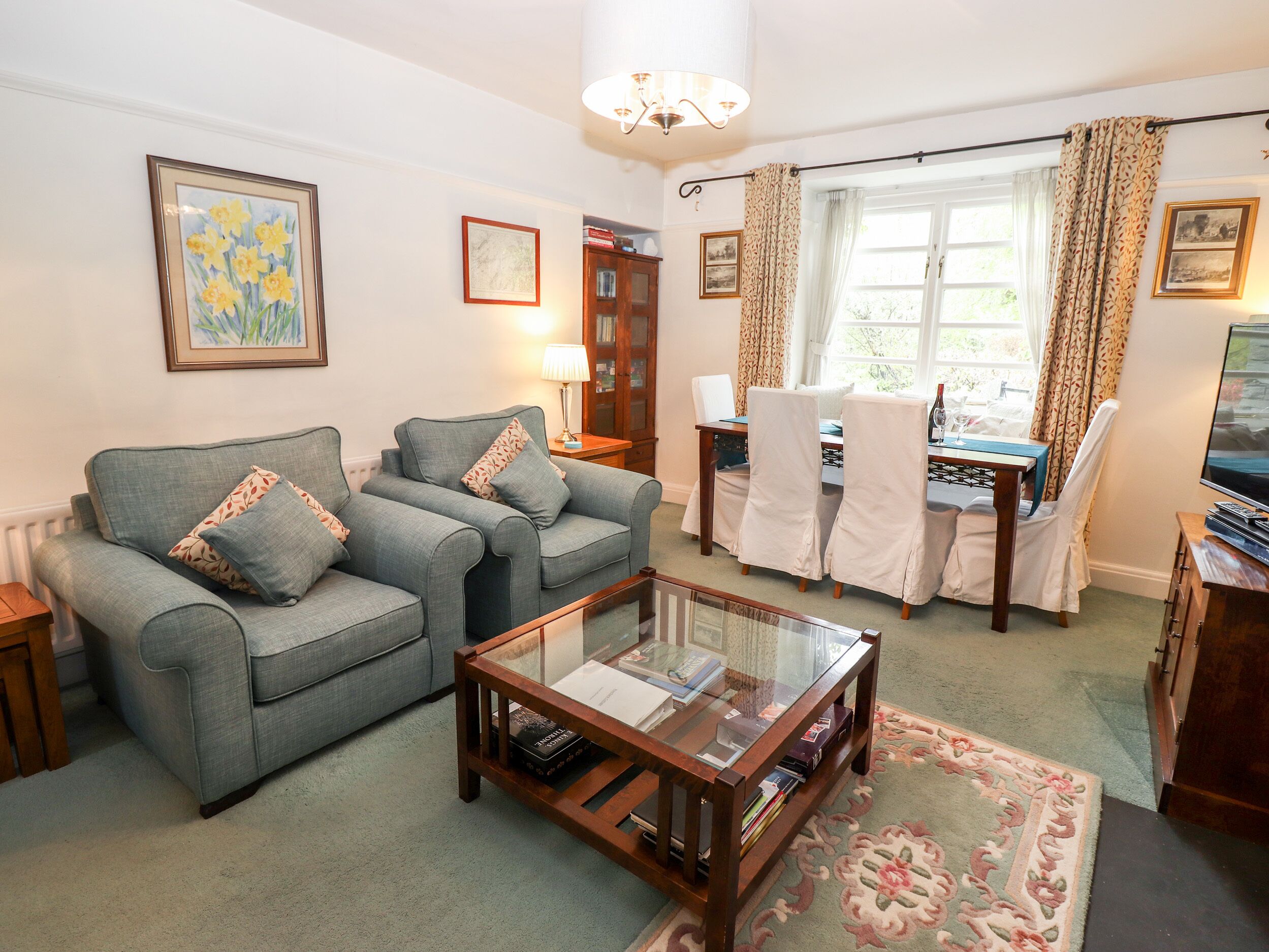 A living room with a sofa set, a glass coffee table, a dining table with chairs, and a television.