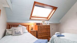 Une chambre avec deux lits, une commode en bois, une table de chevet, une lampe et une lucarne.