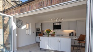 A modern kitchen with white cabinetry, a central island, a built-in oven, and a flat-screen TV. - Salt Bay (Whitby)