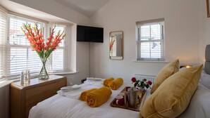 A hotel room with a bed, a bedside table with a vase of flowers, a tray with towels and breakfast items, and a television mounted on the wall. - Salt Bay (Whitby)