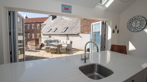 A kitchen with a large island, a sink, and a dining area with outdoor seating. - Salt Bay (Whitby)