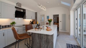 A modern kitchen with a central island, bar stools, and a large window. - Salt Bay (Whitby)