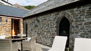A stone building with a wooden deck, wicker furniture, and a glass door. - Frogwell Chapel (Callington)