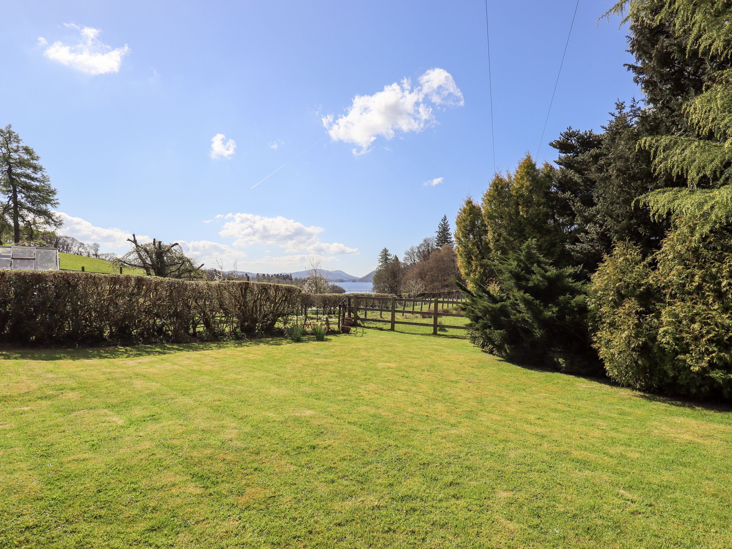 A grassy field with a wooden fence and trees, a clear sky, and distant mountains.