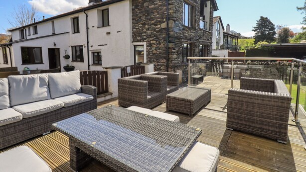A patio area with wicker furniture, a glass balustrade, and a stone building in the background. - Ecclerigg Garth (Windermere)