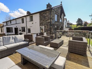Un espace patio aménagé avec des meubles en osier, une balustrade en verre et un bâtiment en pierre en arrière-plan.