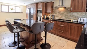 A modern kitchen with a central island, wooden cabinets, stainless steel appliances, and a black countertop. - Ecclerigg Garth (Windermere)