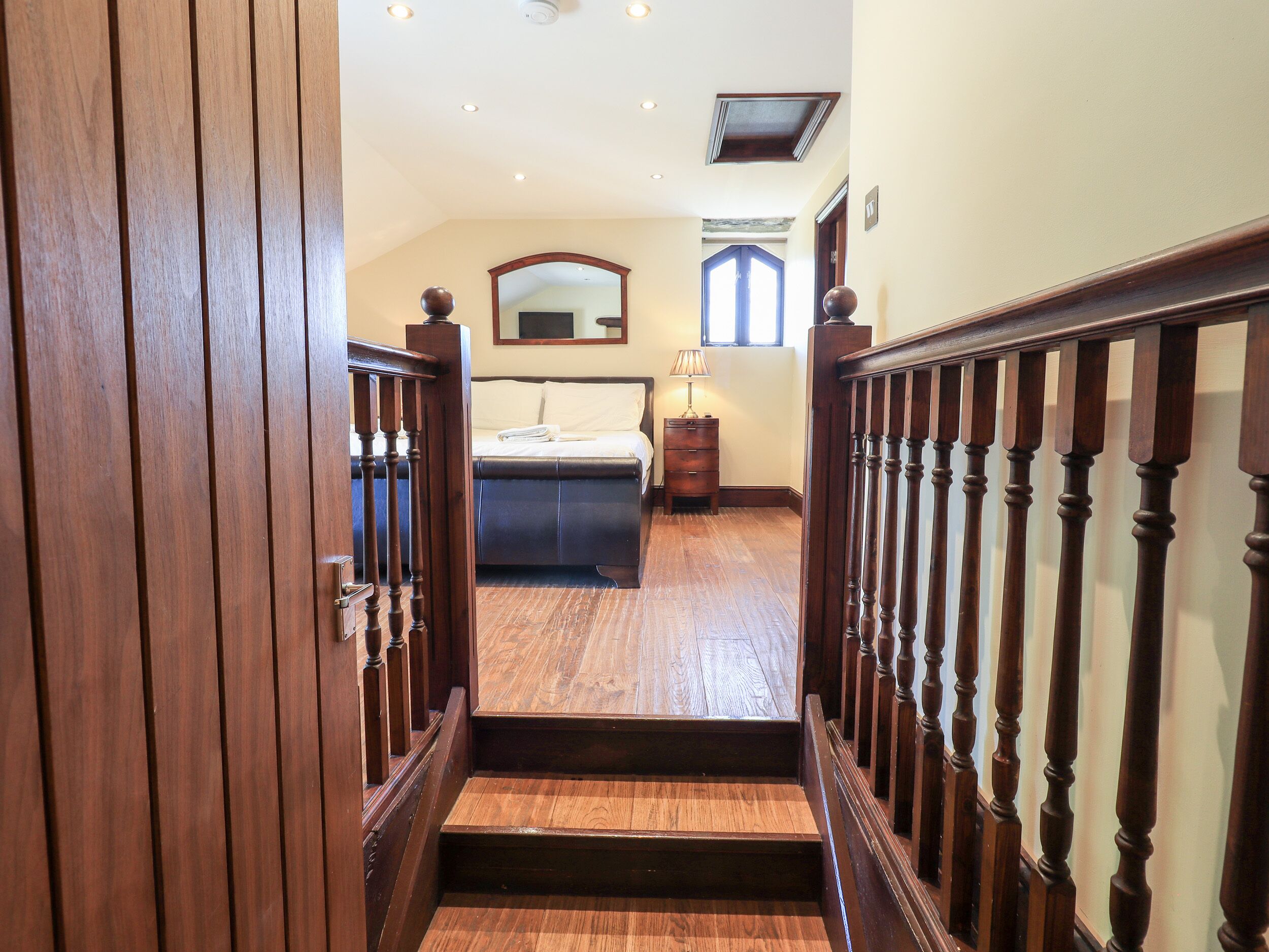 A wooden staircase leading to a bedroom with a bed, a nightstand, and a window.