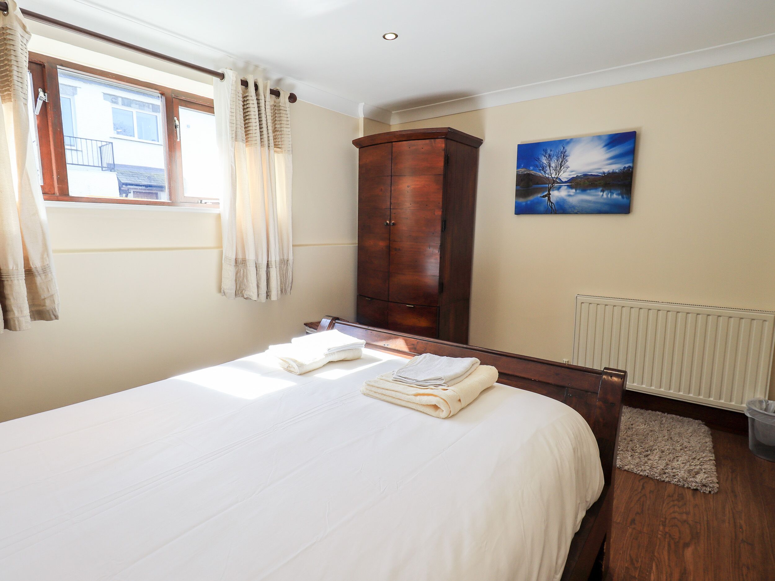 Une chambre à coucher avec un lit, une armoire en bois, un radiateur et une fenêtre avec des rideaux.